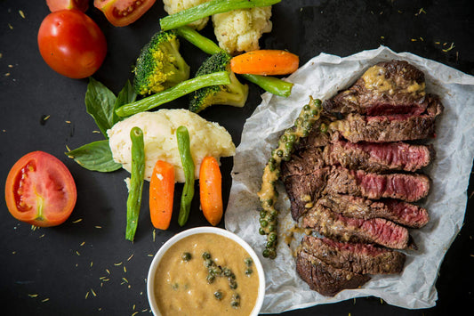 A plate of food featuring a grilled steak, fresh vegetables, and leafy greens, showcasing a balanced, nutrient-rich meal.