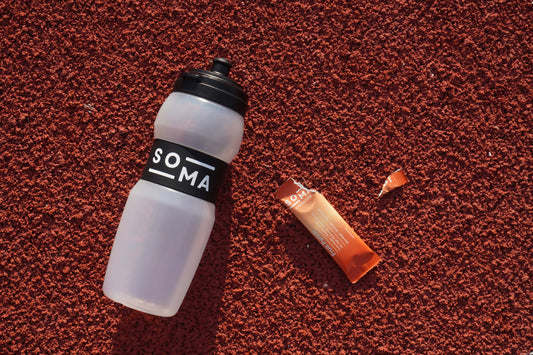 SOMA bottle and opened electrolyte sachet placed on a running track, emphasizing performance hydration during training.